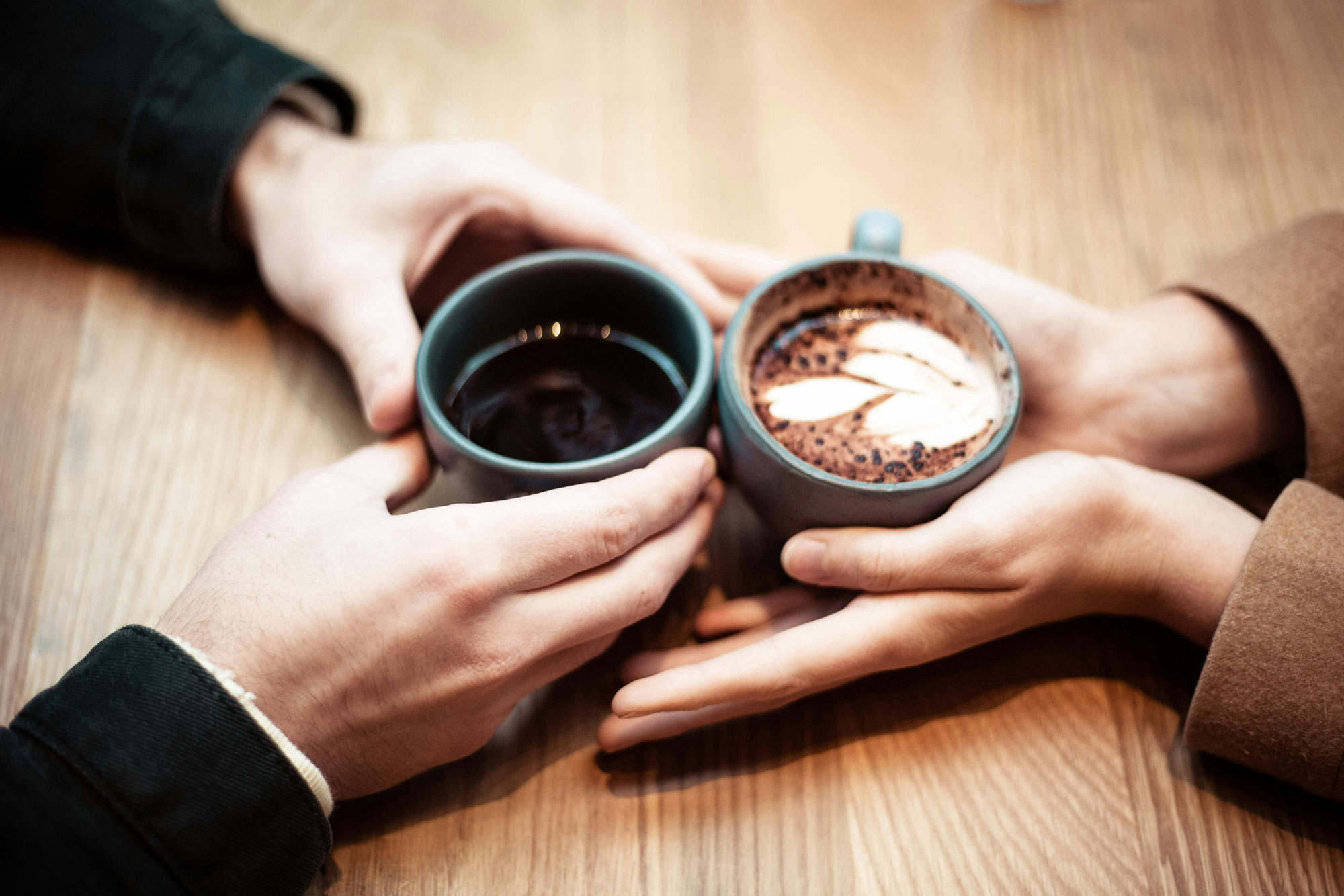 Zwei Hände halten Kaffeetassen über einem Holztisch zusammen