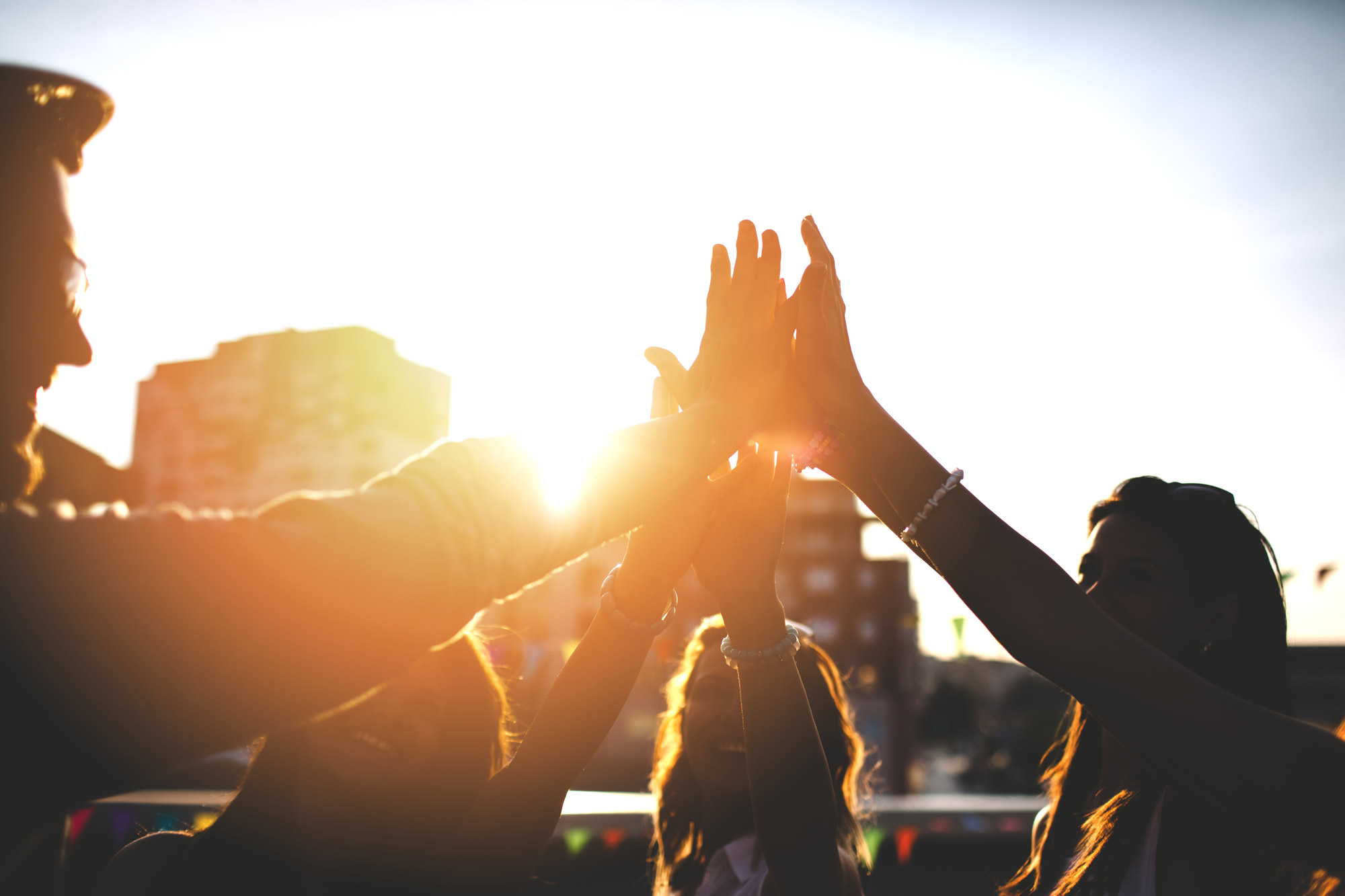 Menschen strecken bei Sonnenuntergang gemeinsam die Hände in die Höhe