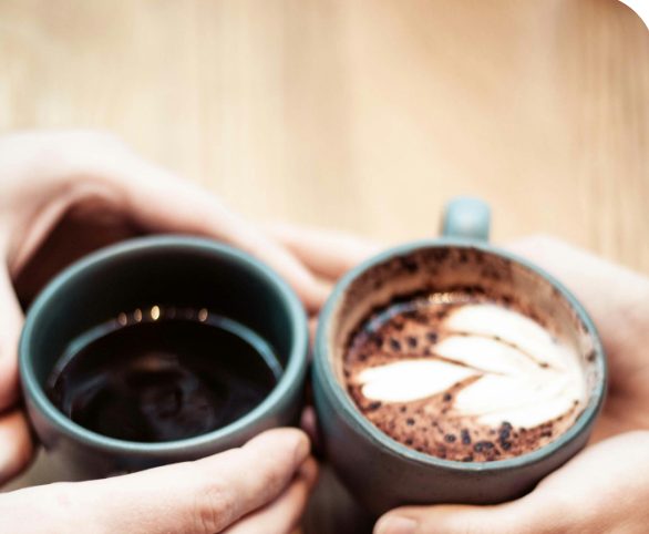 Zwei Hände halten Kaffeetassen über einem Holztisch zusammen