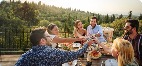 Gruppe stößt an einem reich gedeckten Tisch im Freien mit Weingläsern an